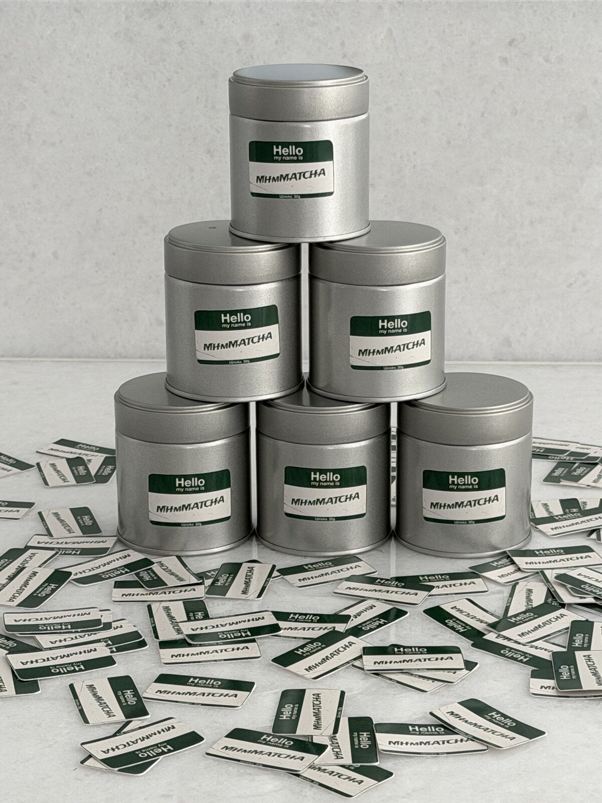 Six MhmMATCHA ceremonial matcha tins stacked in a pyramid with name-tag stickers